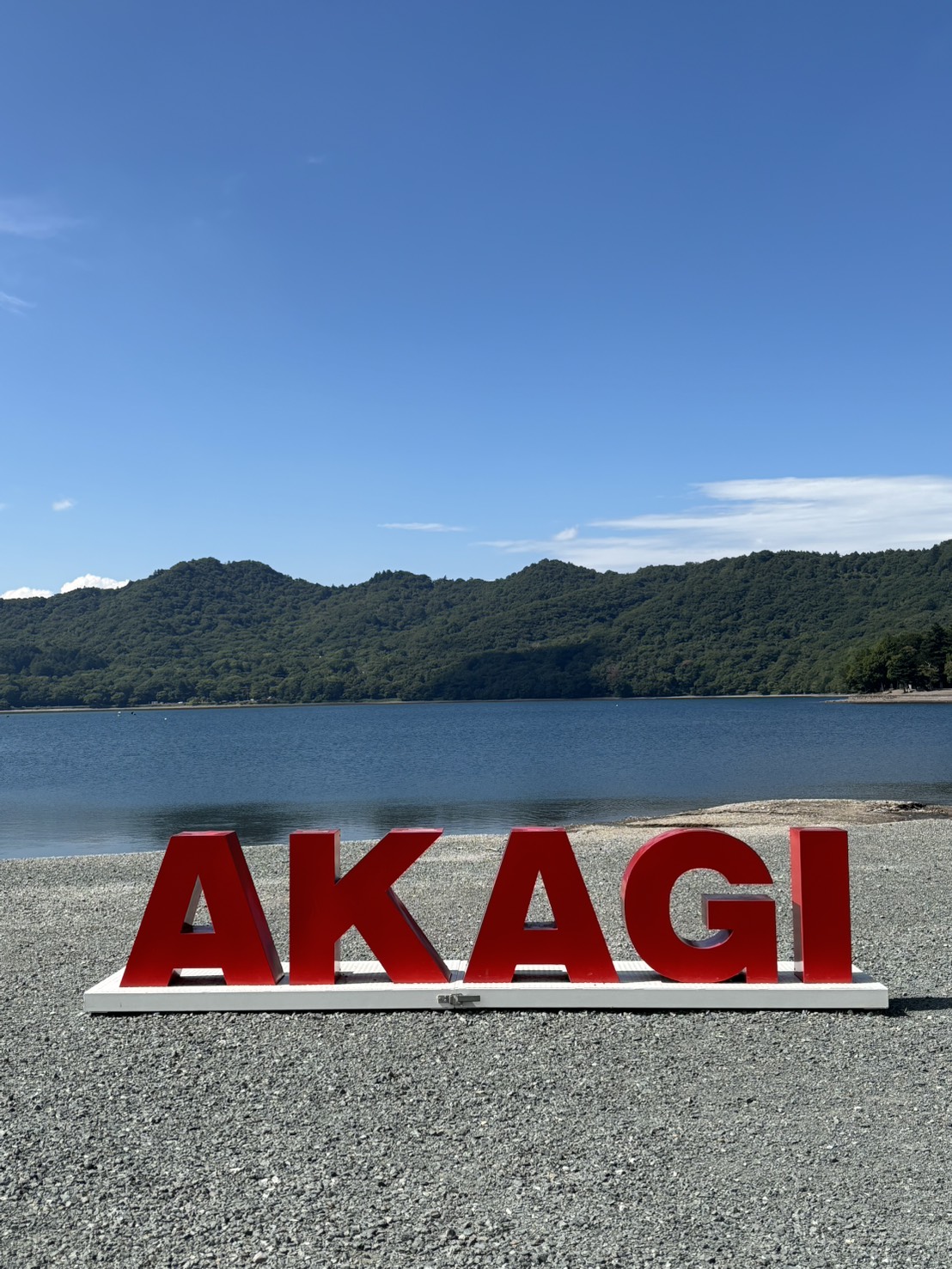 青空の下の大沼と、湖のほとりに置かれた赤い「AKAGI」の文字