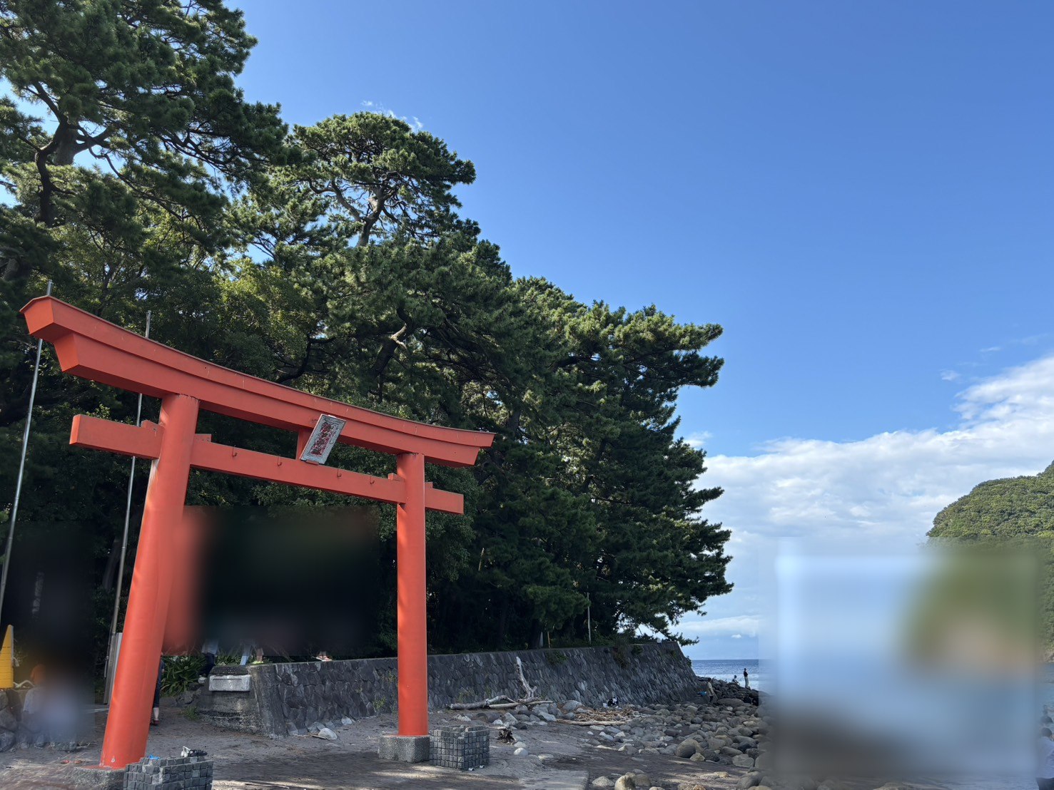 赤い鳥居のむこうに、海と、緑におおわれた岬の崖