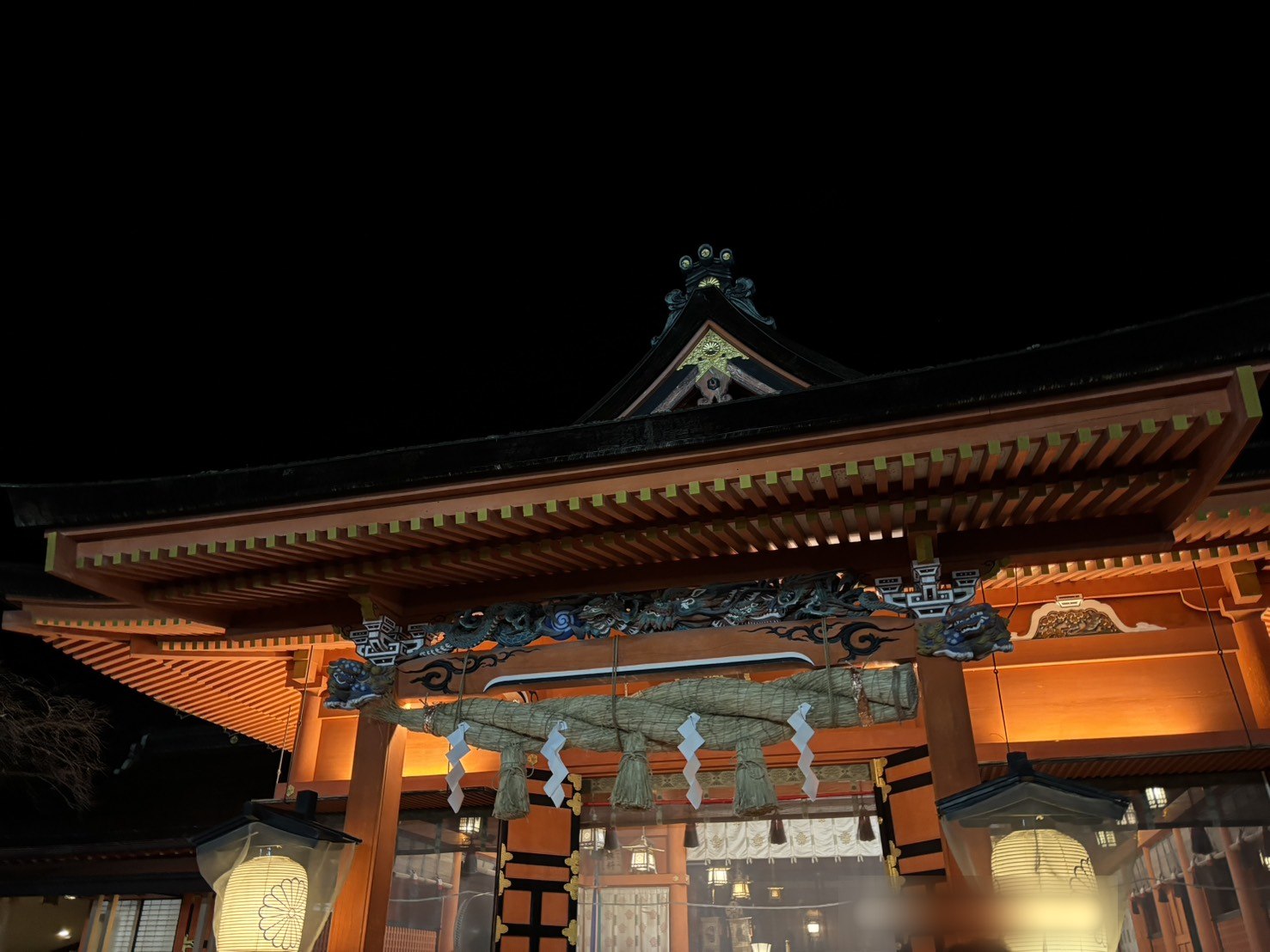 夜の明かりに照らされた、朱色の社殿と大きなしめ縄
