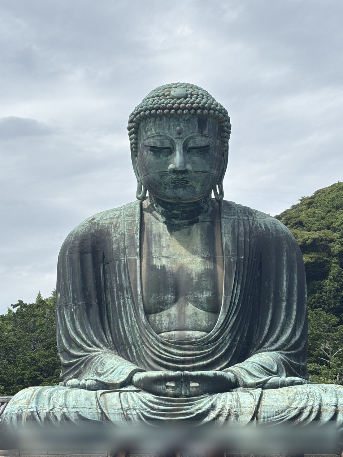 くもり空の下に座る、青緑色の鎌倉の大仏