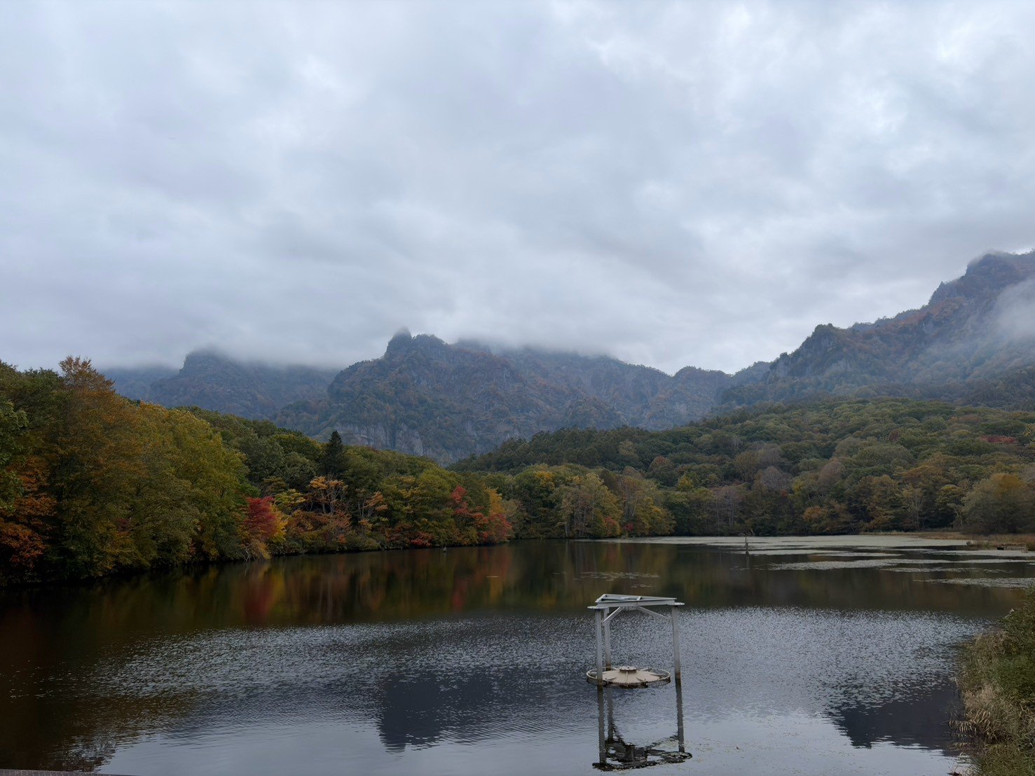 鏡池。水面のむこうに、紅葉した森と、雲のかかった戸隠の山が見える