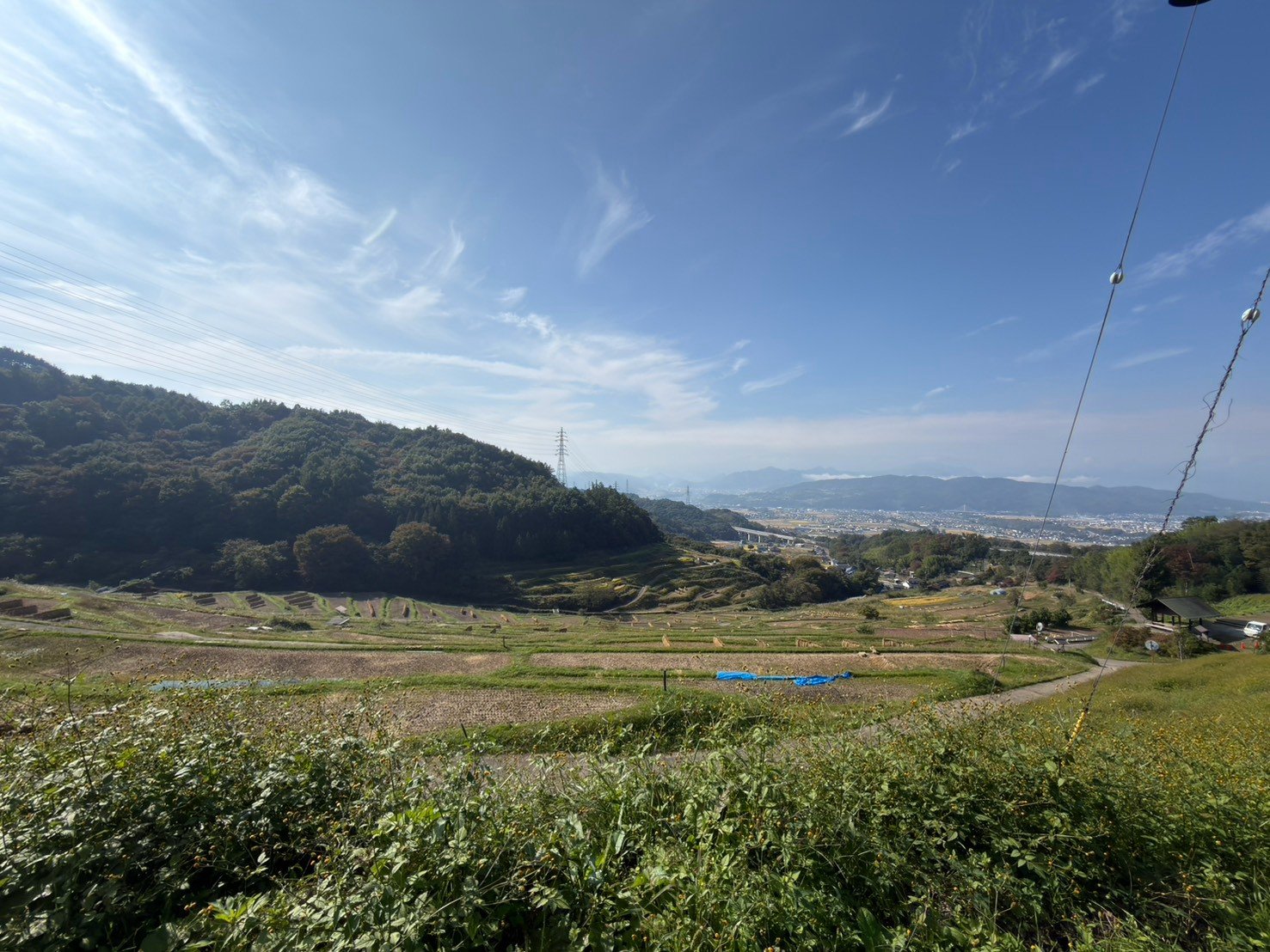 山の斜面の棚田から、遠くの町と山並みを見下ろした景色