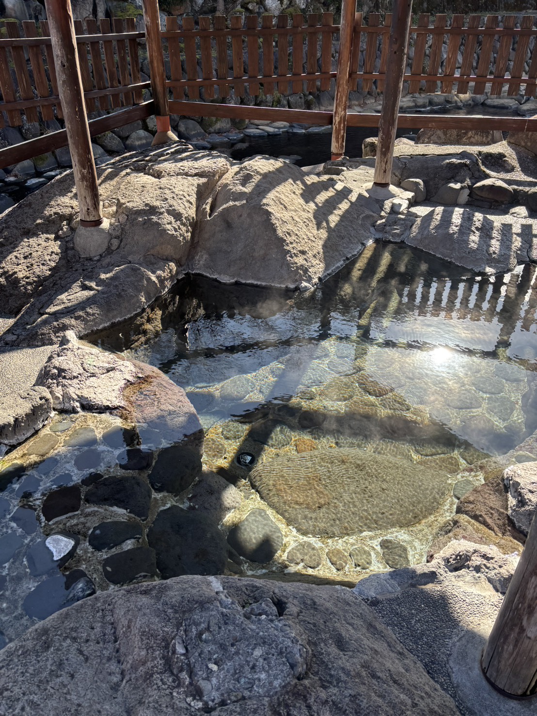 岩にかこまれた温泉。湯気が立ち、水の底の石が透けて見える